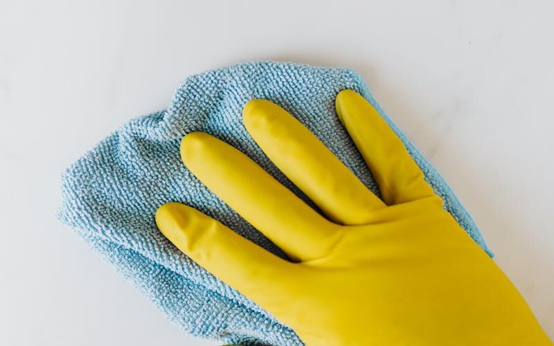 Yellow gloved hand wiping surface with blue cloth, concept of cleaning and hygiene.